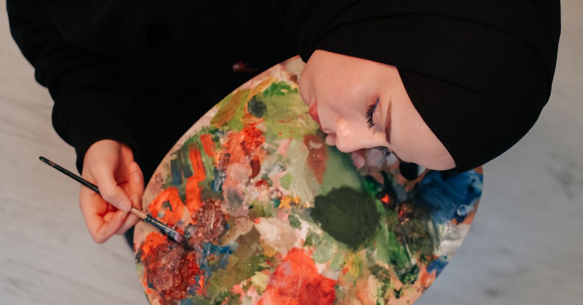 A woman in a hijab paints with a vibrant palette, focusing on her artwork.